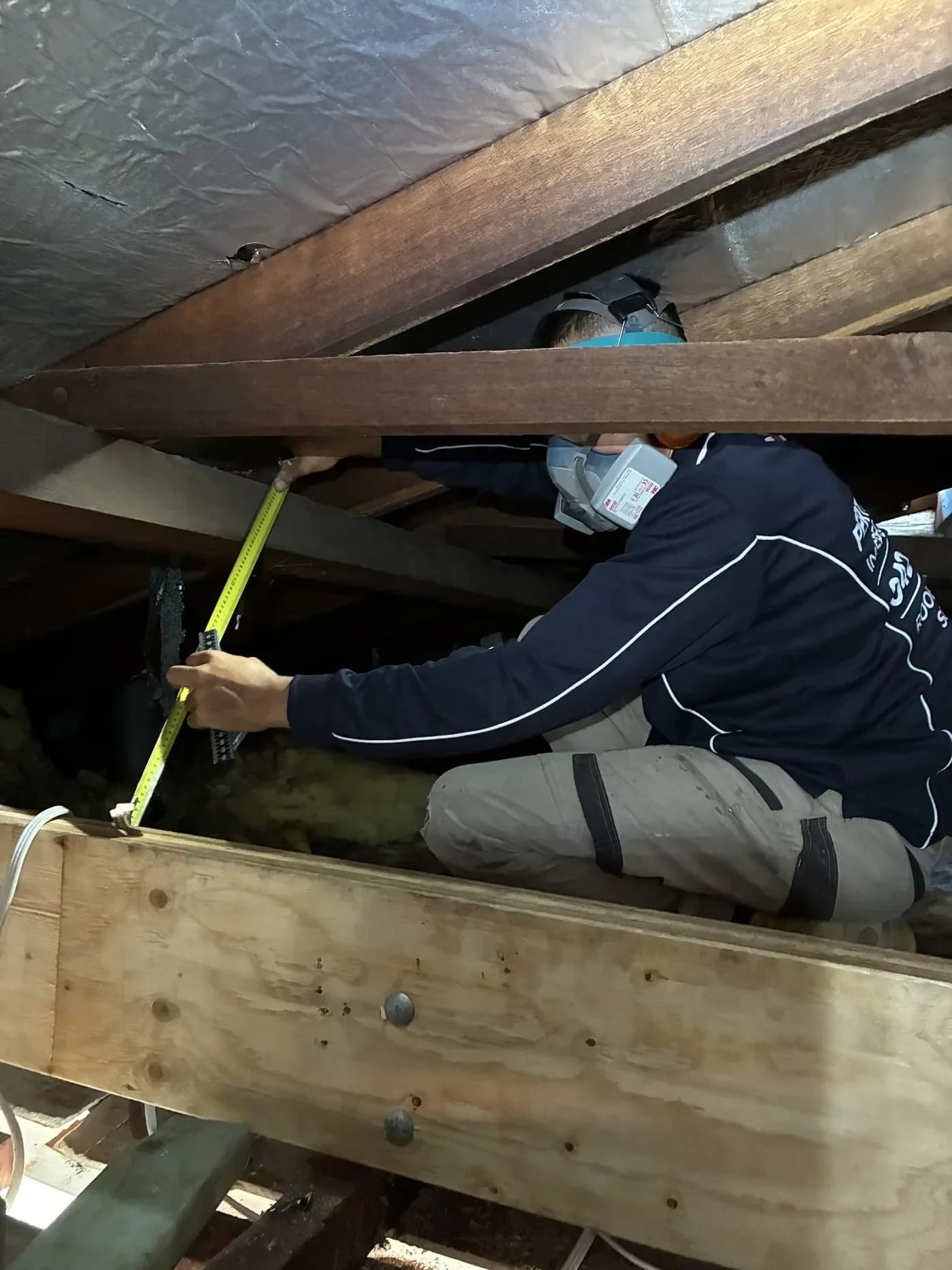 A tradesperson measuring roof timbers inside the cavity